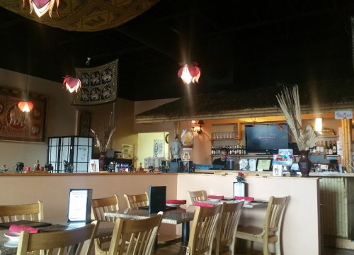 Interior of a cozy restaurant featuring wooden tables, decorative lighting, and a bar area with various bottles.