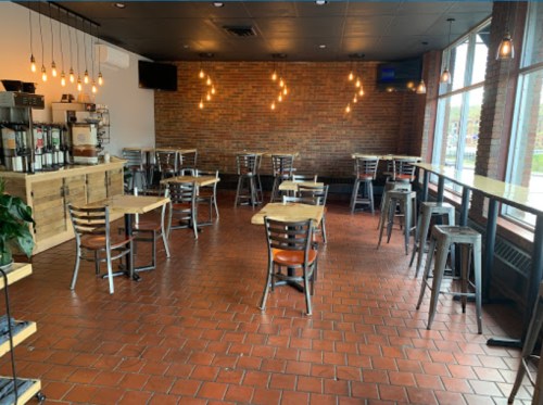 A cozy restaurant interior with wooden tables, metal chairs, and warm lighting against a brick wall.