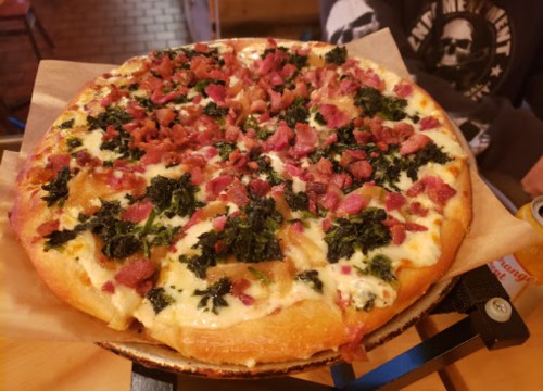 A freshly baked pizza topped with cheese, bacon, and kale on a wooden serving tray.