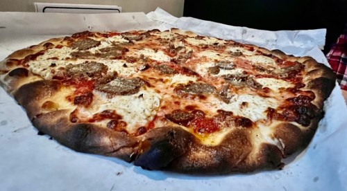 A large pizza with melted cheese, sausage toppings, and a golden-brown crust on a white paper surface.