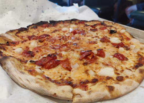 A freshly baked pizza topped with pepperoni and cheese, resting on a white paper-lined tray.