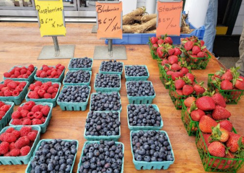 Baskets of raspberries, blueberries, and strawberries for sale at a market, with prices displayed.