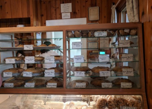 Display case filled with various baked goods, including pies and cookies, labeled with names and prices.