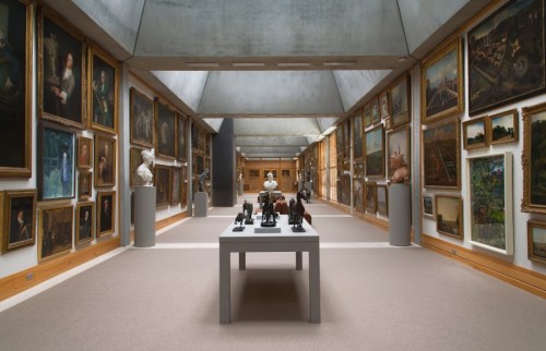 A spacious art gallery with framed paintings on the walls and sculptures displayed on a central table.