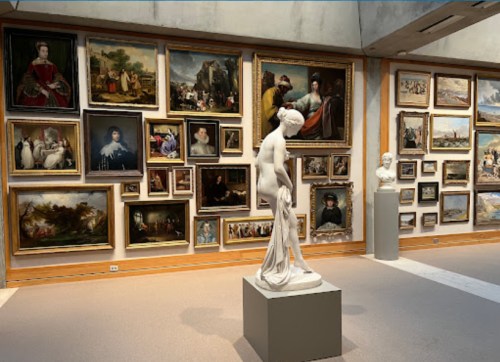 A gallery interior featuring a white statue in front of various framed paintings on the walls.