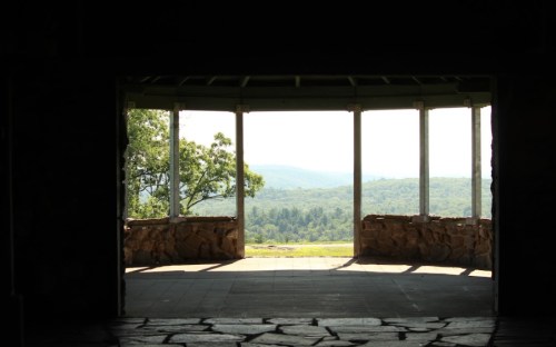 View through an open structure, showcasing a scenic landscape of rolling hills and trees in the distance.