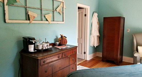 Cozy room with blue walls, a wooden dresser, coffee station, and a vintage wardrobe, decorated with a bunting banner.