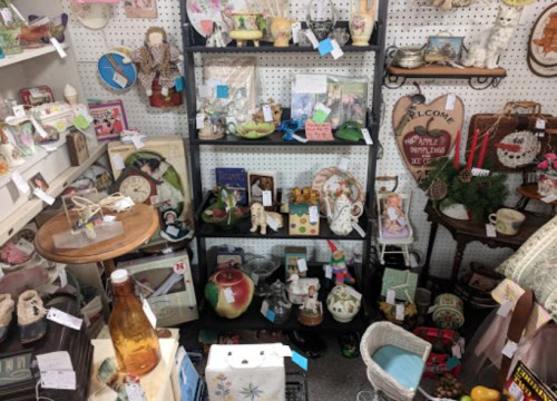 A cluttered display of vintage items, including dolls, decor, and collectibles on shelves and tables.