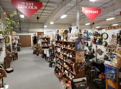 A spacious antique shop aisle with shelves filled with various vintage items, labeled "West Lincoln" and "Bethany."