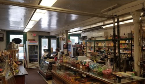 A cozy store interior with shelves of products, a glass display case, and a cashier at the counter.