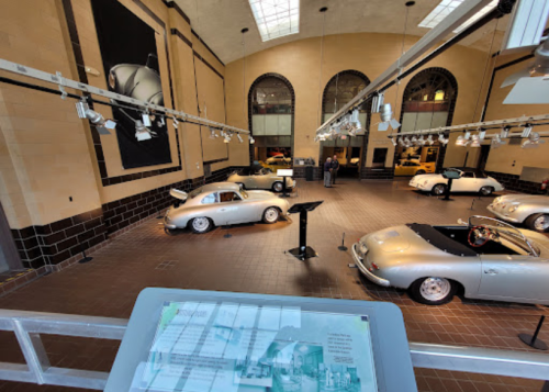 A spacious museum gallery featuring several vintage silver cars and informational displays.