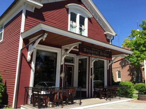 A charming red general store with a sign, outdoor seating, and a clear blue sky in the background.