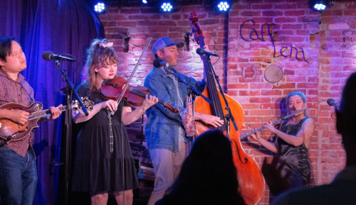 A lively band performs on stage at Caffe Lena, featuring a mandolin, violin, double bass, and flute.