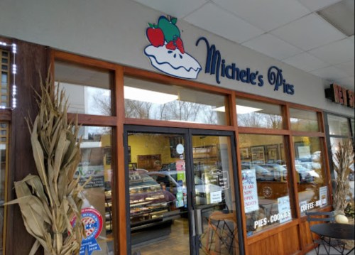 Exterior of Michele's Pies shop, featuring a sign with a pie graphic and large windows displaying baked goods inside.