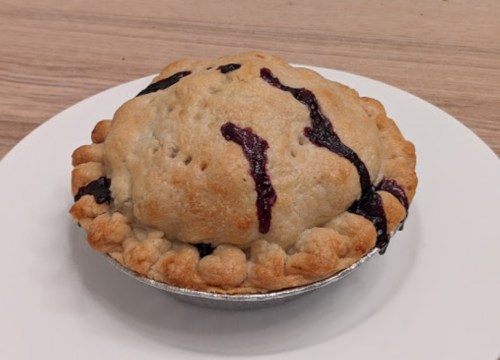 A freshly baked pie with a golden crust and berry filling, sitting on a white plate against a wooden background.
