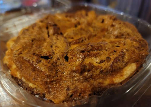 A close-up of a baked pie with a golden-brown, textured crust in a clear plastic container.