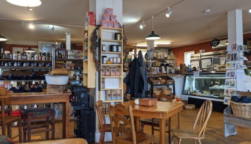 A cozy shop interior with wooden tables, shelves of jars, and various items for sale, creating a warm atmosphere.