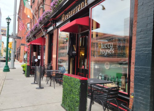 Exterior of Kitty Hoyne's restaurant with outdoor seating, planters, and Irish flags on a city street.