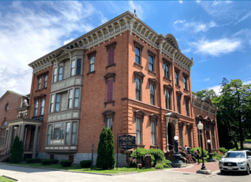 Historic brick building with ornate architecture, surrounded by greenery and a clear blue sky.