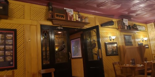 Interior of a cozy restaurant with yellow walls, wooden furniture, and decorative items on shelves.