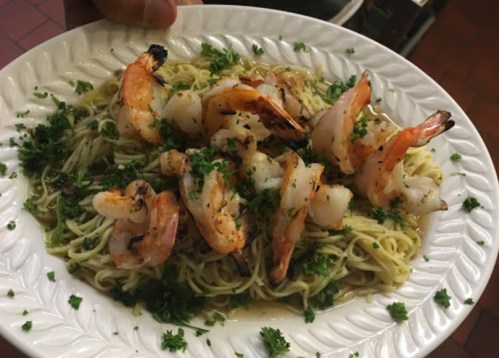 A plate of pasta topped with grilled shrimp and garnished with parsley.