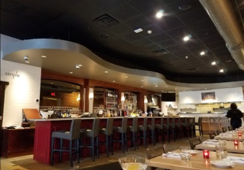 A modern restaurant interior featuring a bar, high stools, and a dining area with soft lighting and a sleek design.