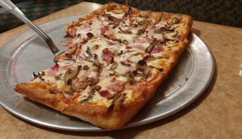 A rectangular pizza topped with cheese, ham, and mushrooms on a metal serving tray.