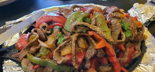 Sizzling fajitas with strips of beef, bell peppers, and onions served on a cast iron skillet.
