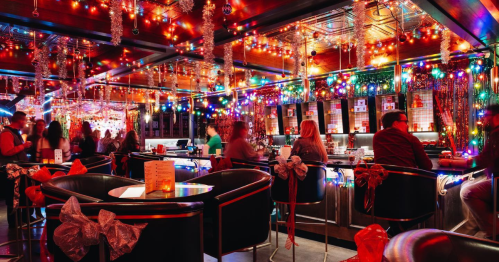 A festive bar decorated with colorful lights and ribbons, filled with people enjoying drinks and conversation.