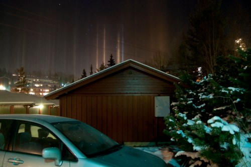 A wooden cabin at night, surrounded by snow, with light pillars shining in the sky above.