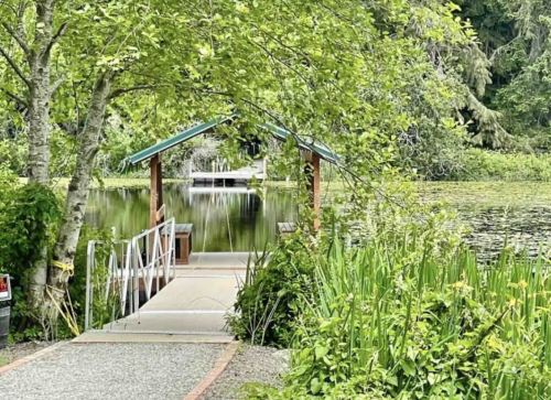 A serene dock leads to a calm lake, surrounded by lush greenery and trees.