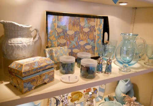 A display of decorative kitchenware, including glassware, jars, and a patterned tray, in shades of blue and cream.