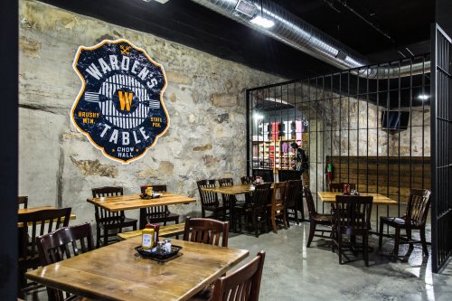 Interior of a restaurant with wooden tables and chairs, featuring a large wall sign that reads "Warden's Table."
