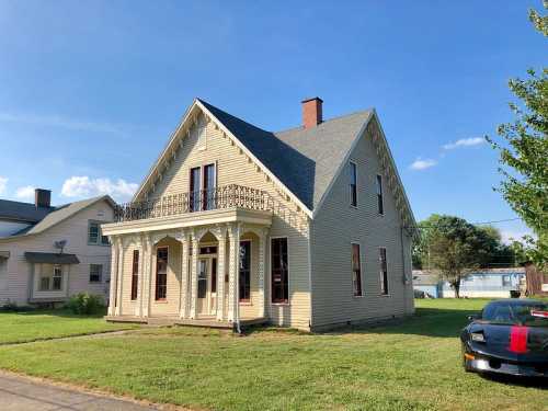 A two-story yellow house with a decorative porch and green lawn, under a clear blue sky.