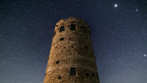 A stone tower stands against a starry night sky, illuminated by distant stars and a bright planet.