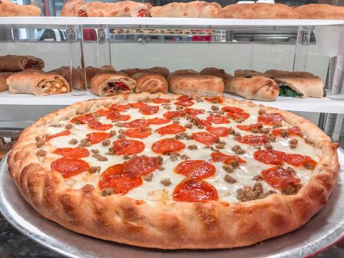 A large pepperoni and sausage pizza on a silver tray, with calzones displayed in the background.