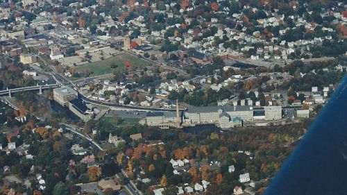 Aerial view of a town with a river, buildings, and autumn foliage, showcasing a mix of urban and natural landscapes.