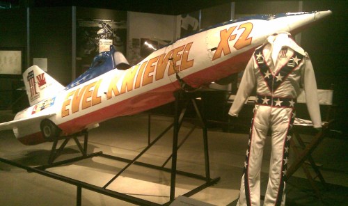 Evel Knievel's X2 rocket motorcycle displayed alongside a white jumpsuit with red and blue star designs.