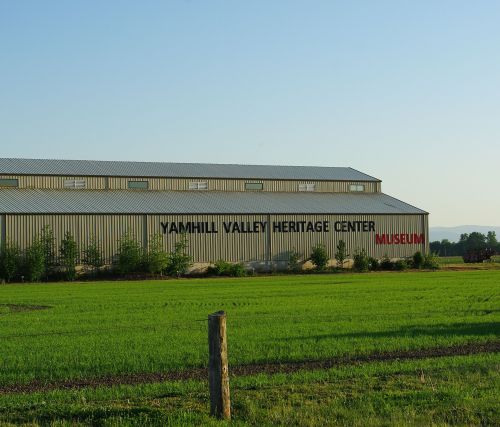 A large metal building with "Yamhill Valley Heritage Center Museum" written on the side, surrounded by green fields.