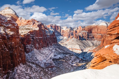 A stunning view of snow-dusted red rock canyons under a blue sky with fluffy clouds in Zion National Park.