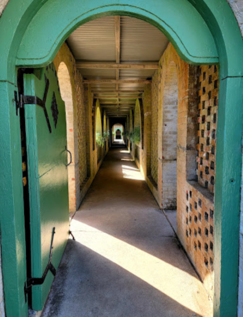 A green arched doorway leads into a sunlit corridor with brick walls and arches, creating a serene atmosphere.