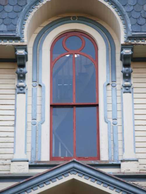 A decorative arched window with red trim and blue accents on a vintage building.