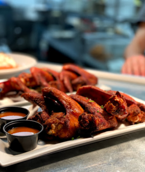 A platter of crispy chicken wings served with two small cups of dipping sauce.