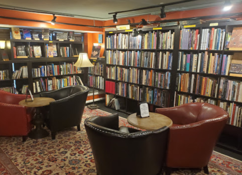 Cozy library corner with two armchairs, a small table, and shelves filled with books against a vibrant orange wall.