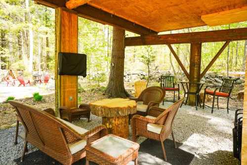 Cozy outdoor seating area with wicker chairs and a wooden table, surrounded by trees and greenery.