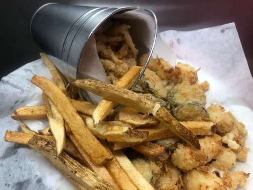 A metal cup tipped over, spilling fried seafood and crispy fries onto a white paper-lined tray.