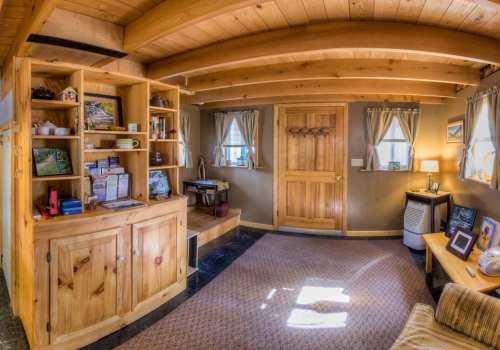 Cozy interior of a wooden cabin with shelves, a door, and natural light streaming through windows.