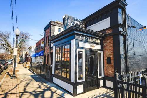 Exterior of a gastropub with large windows, a black and brick facade, and a clear blue sky in the background.