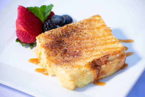 A slice of dessert drizzled with caramel, served with strawberries, blueberries, and blackberries on a white plate.