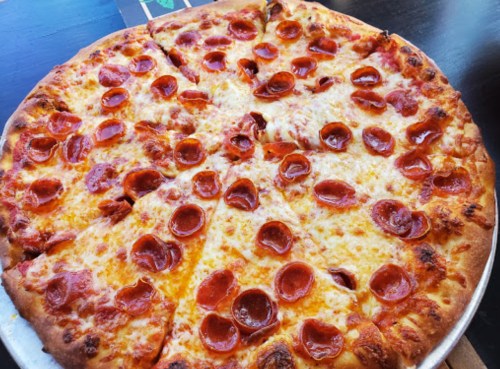 A large pepperoni pizza with melted cheese and a golden crust, sliced into eight pieces.